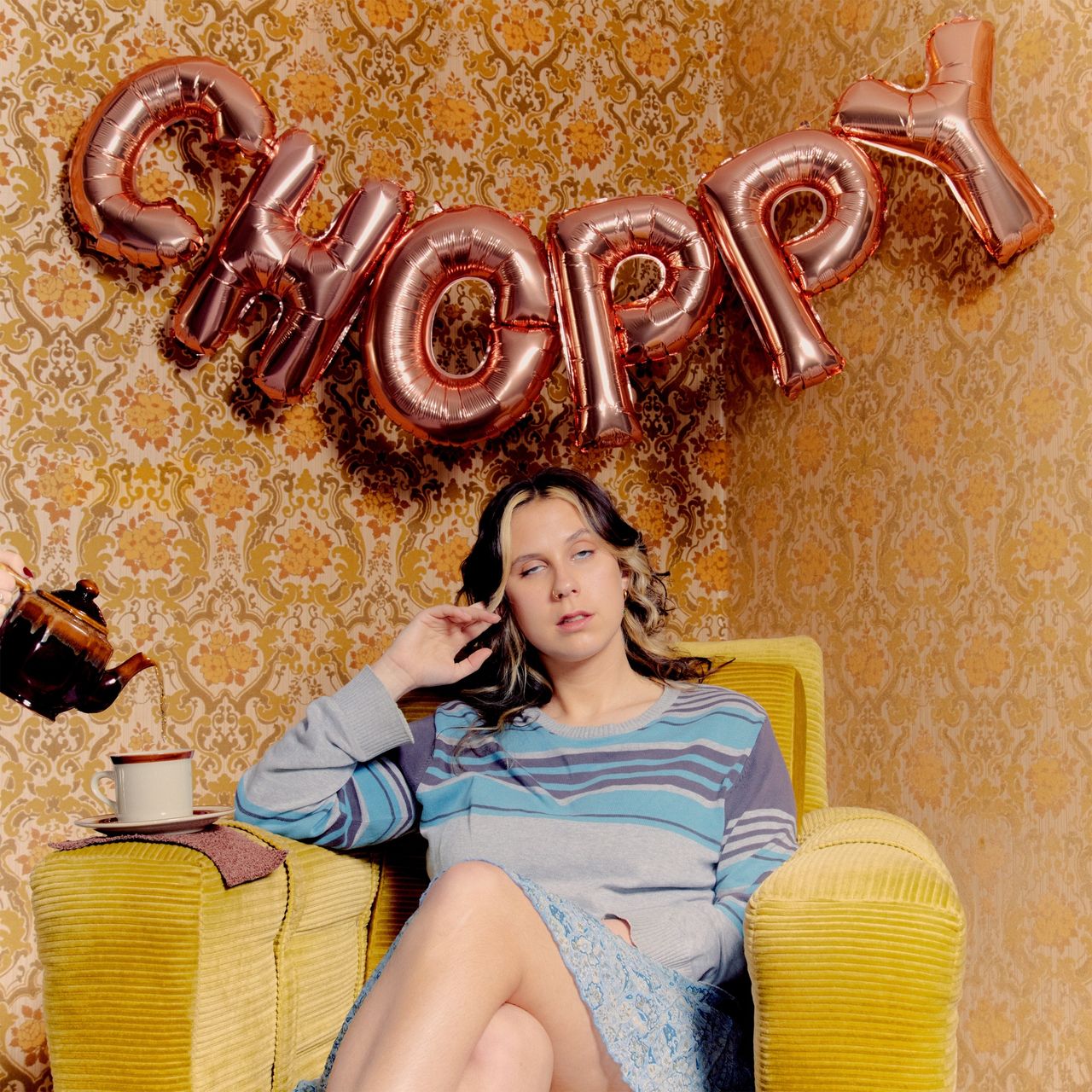 Album cover for Grace Robinson's Choppy: singer sits in a yellow armchair under foil balloons spelling 'choppy' as tea is poured into a mug.